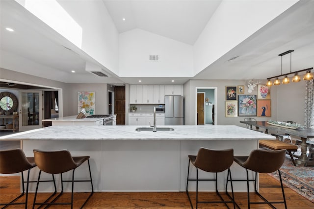 kitchen with white cabinets, a kitchen breakfast bar, light stone countertops, decorative light fixtures, and stainless steel refrigerator