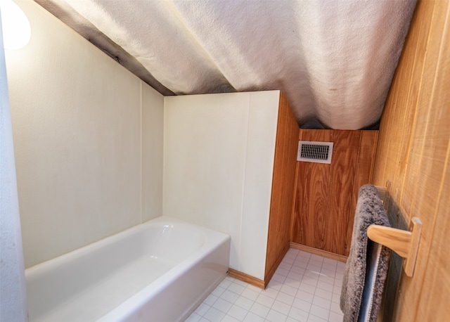 bathroom with a bathing tub, wooden walls, tile patterned flooring, and a textured ceiling