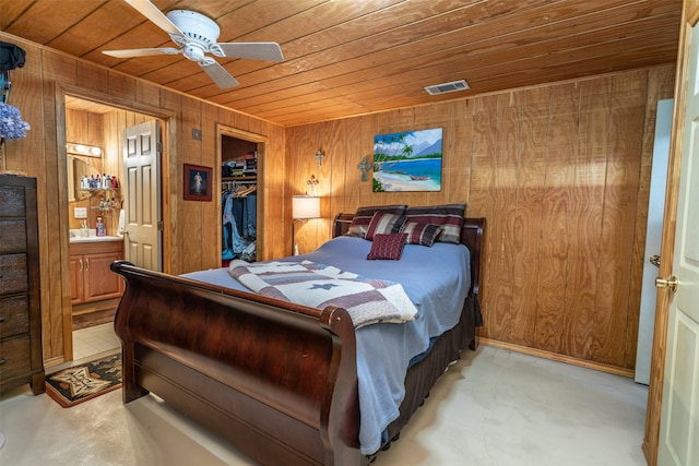 bedroom featuring wood ceiling, connected bathroom, a closet, ceiling fan, and wooden walls