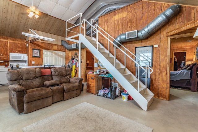 living room featuring ceiling fan, wooden walls, and concrete floors