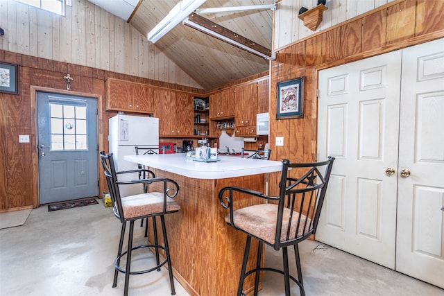 kitchen with kitchen peninsula, white appliances, wooden walls, high vaulted ceiling, and a kitchen breakfast bar