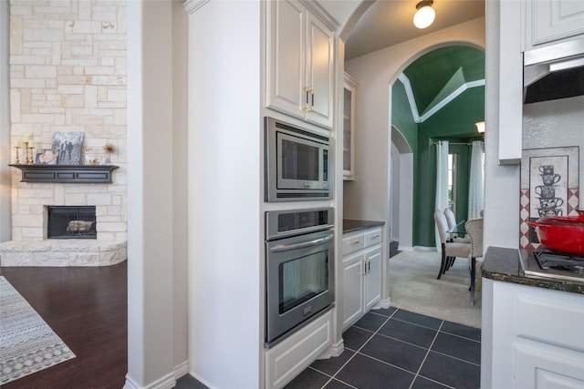 kitchen with white cabinetry, appliances with stainless steel finishes, dark tile patterned floors, and a fireplace