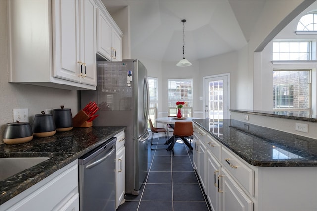 kitchen with white cabinetry, dark tile patterned flooring, hanging light fixtures, dark stone counters, and stainless steel dishwasher