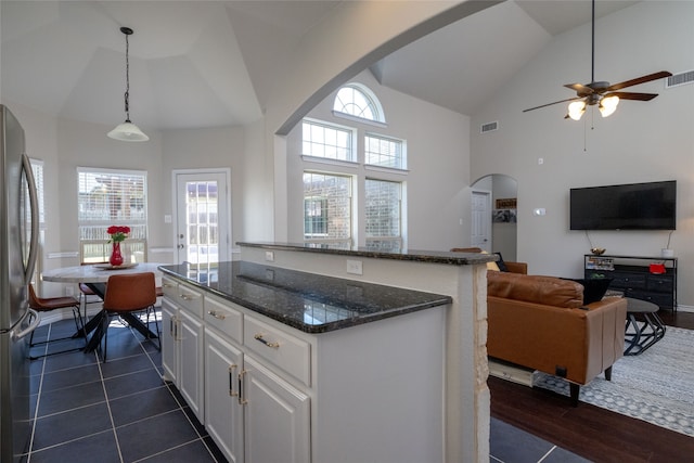 kitchen featuring dark stone countertops, a kitchen island, pendant lighting, white cabinetry, and stainless steel fridge