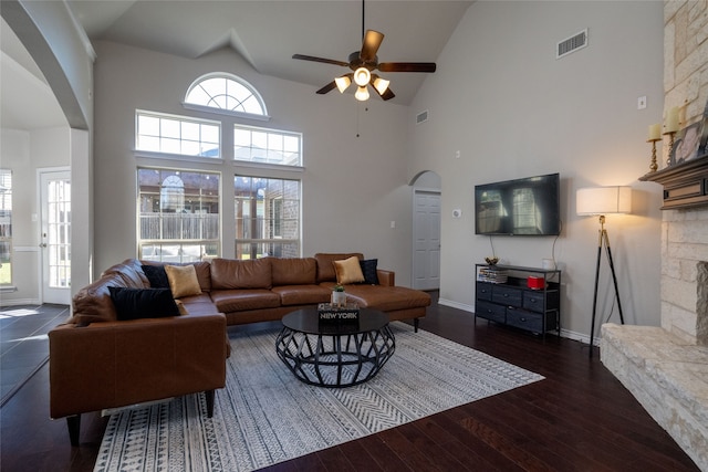 living room with ceiling fan, dark wood-type flooring, a towering ceiling, and a fireplace