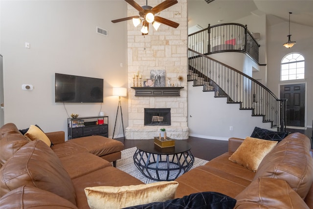 living room with ceiling fan, hardwood / wood-style flooring, a stone fireplace, and high vaulted ceiling