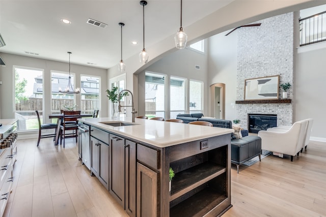 kitchen featuring a large fireplace, a kitchen island with sink, sink, pendant lighting, and light hardwood / wood-style floors