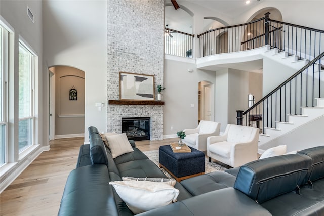 living room featuring a healthy amount of sunlight, a fireplace, a towering ceiling, and light hardwood / wood-style floors