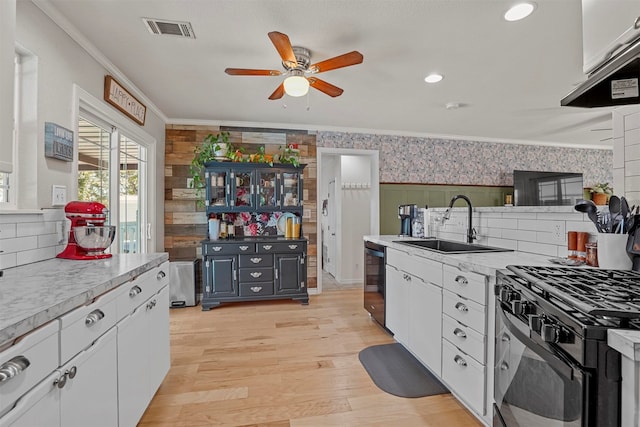 kitchen with white cabinets, black appliances, sink, ornamental molding, and light hardwood / wood-style floors