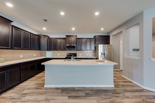 kitchen with stainless steel appliances, sink, a kitchen island with sink, light hardwood / wood-style flooring, and dark brown cabinets