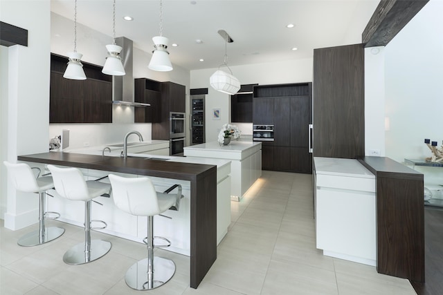 kitchen with a breakfast bar, pendant lighting, wall chimney range hood, and kitchen peninsula