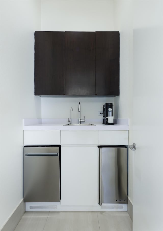 bar featuring stainless steel dishwasher, white cabinets, sink, and light tile patterned flooring