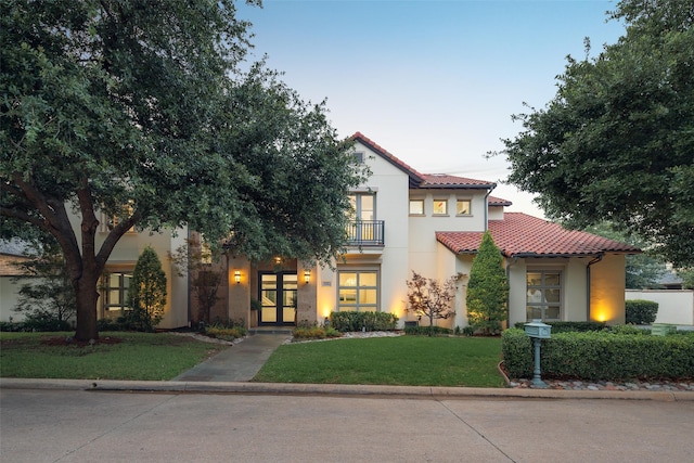 mediterranean / spanish house featuring a balcony, a yard, and french doors