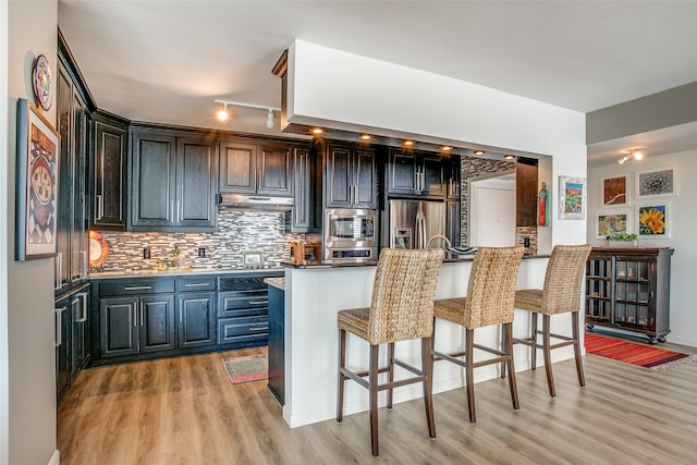 kitchen featuring appliances with stainless steel finishes, decorative backsplash, a breakfast bar, kitchen peninsula, and light wood-type flooring