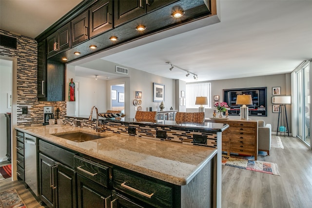 kitchen with sink, a center island with sink, backsplash, light stone countertops, and light hardwood / wood-style floors