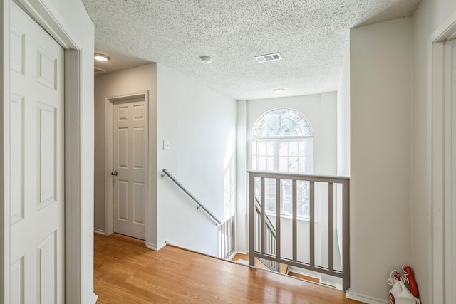 hall with a textured ceiling and light hardwood / wood-style flooring