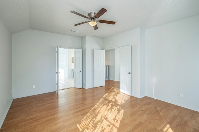 unfurnished bedroom featuring lofted ceiling, a textured ceiling, light wood-type flooring, and ceiling fan