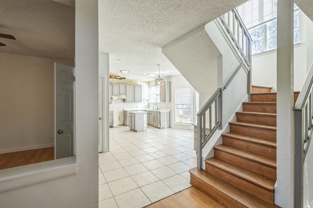 staircase with a textured ceiling, sink, tile patterned floors, and a wealth of natural light