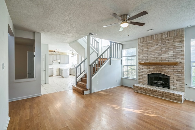 unfurnished living room with ceiling fan, a textured ceiling, light wood-type flooring, and a fireplace