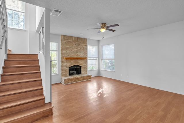 unfurnished living room with light hardwood / wood-style floors, a textured ceiling, a brick fireplace, and ceiling fan