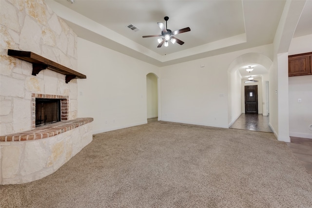 unfurnished living room with a tray ceiling, ceiling fan, carpet flooring, and a stone fireplace