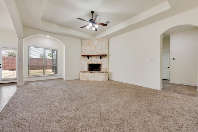 unfurnished living room featuring ceiling fan, a raised ceiling, a fireplace, and light tile patterned floors