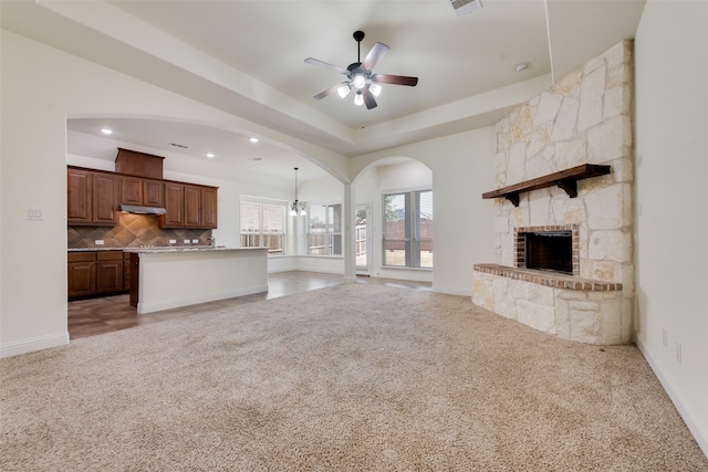 unfurnished living room featuring a stone fireplace, ceiling fan, and light colored carpet