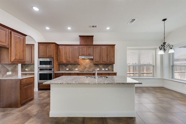 kitchen with an island with sink, decorative backsplash, stainless steel appliances, and light stone counters