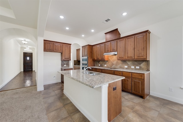 kitchen featuring appliances with stainless steel finishes, decorative backsplash, an island with sink, light stone countertops, and sink