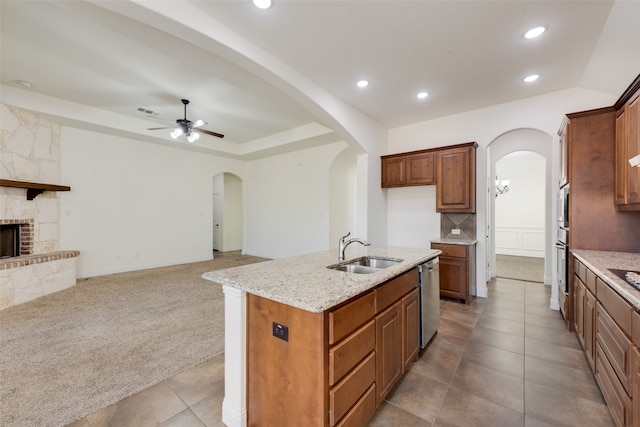 kitchen with a kitchen island with sink, sink, a fireplace, light carpet, and ceiling fan