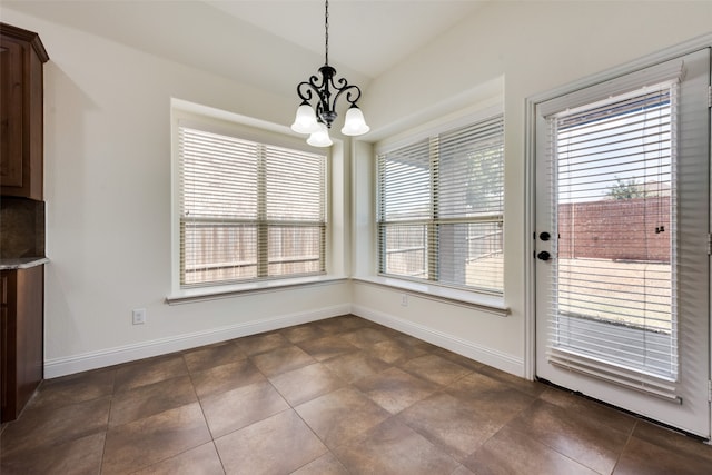 unfurnished dining area with an inviting chandelier, dark tile patterned floors, and a wealth of natural light