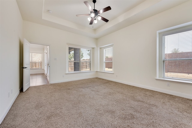 unfurnished bedroom with ceiling fan, a raised ceiling, and light carpet