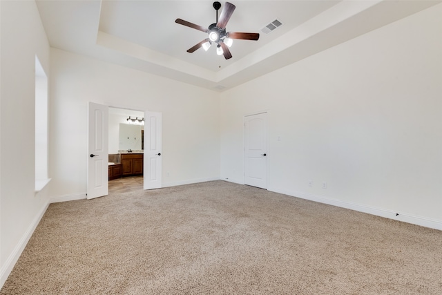 unfurnished bedroom with a raised ceiling, ensuite bath, ceiling fan, and light colored carpet