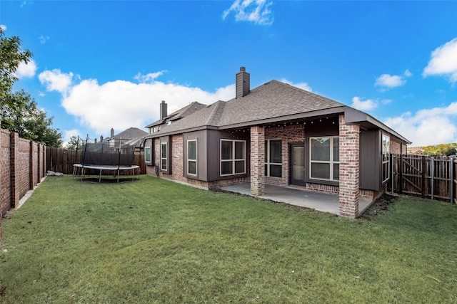 back of property with a trampoline, a yard, and a patio