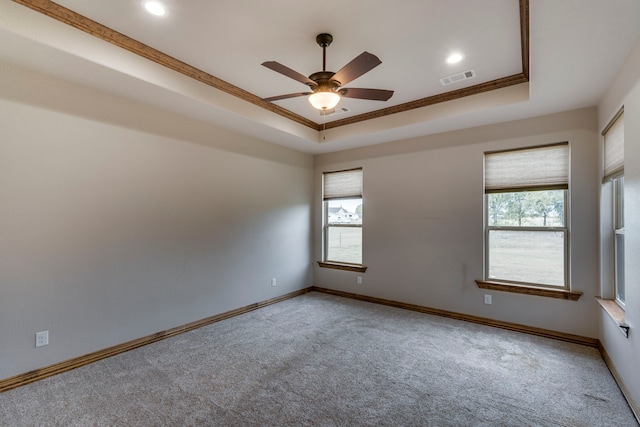 carpeted spare room featuring ceiling fan, a raised ceiling, plenty of natural light, and ornamental molding