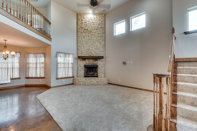 unfurnished living room featuring ceiling fan with notable chandelier, a high ceiling, concrete flooring, and a stone fireplace