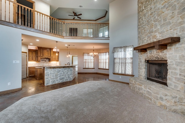 unfurnished living room featuring ceiling fan with notable chandelier, a stone fireplace, and a towering ceiling