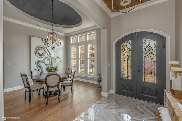 foyer entrance featuring a raised ceiling, french doors, ornamental molding, hardwood / wood-style floors, and a chandelier