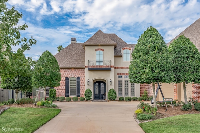 french country inspired facade with french doors, a balcony, and a front yard