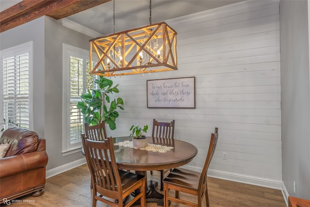 dining room featuring wood walls, beamed ceiling, crown molding, wood-type flooring, and a notable chandelier