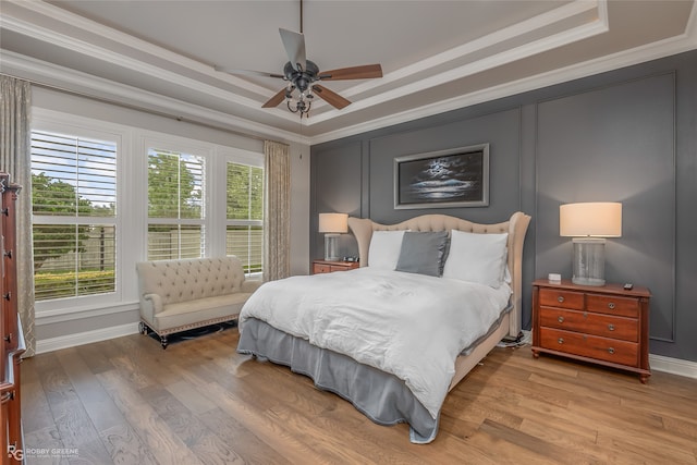 bedroom featuring light wood-type flooring, a tray ceiling, ceiling fan, and crown molding