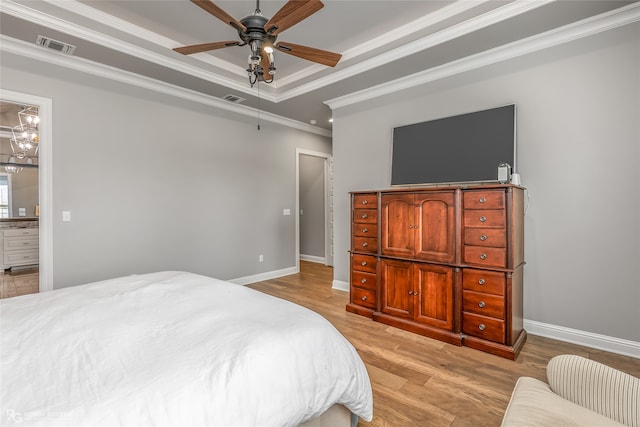 bedroom featuring a tray ceiling, ceiling fan with notable chandelier, light hardwood / wood-style flooring, ensuite bath, and crown molding