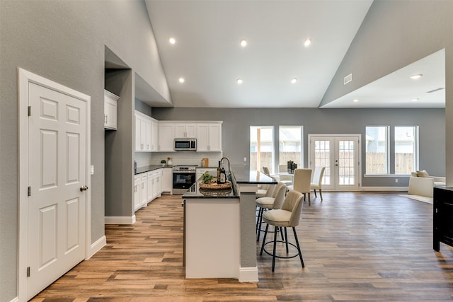 kitchen with appliances with stainless steel finishes, white cabinets, light hardwood / wood-style flooring, french doors, and a kitchen island with sink