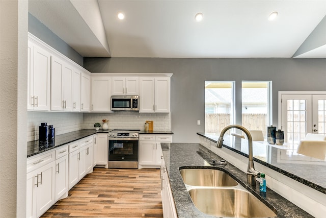 kitchen with light wood-type flooring, tasteful backsplash, sink, white cabinetry, and appliances with stainless steel finishes