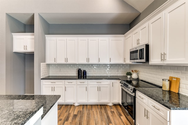 kitchen with appliances with stainless steel finishes, dark stone countertops, light wood-type flooring, and white cabinets