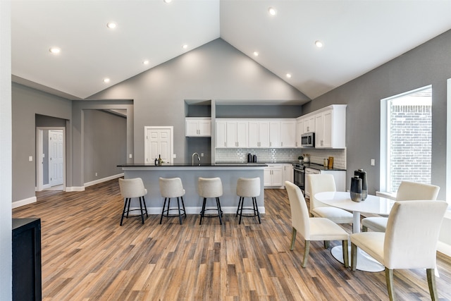 kitchen with hardwood / wood-style flooring, an island with sink, white cabinetry, high vaulted ceiling, and stainless steel appliances