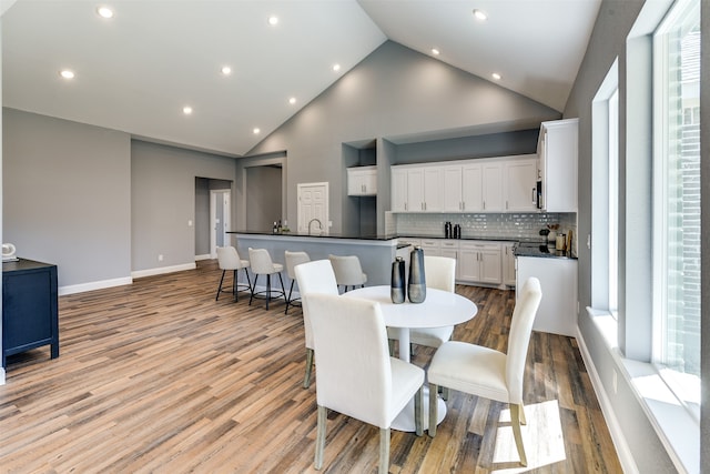 dining area with sink, light hardwood / wood-style floors, and high vaulted ceiling