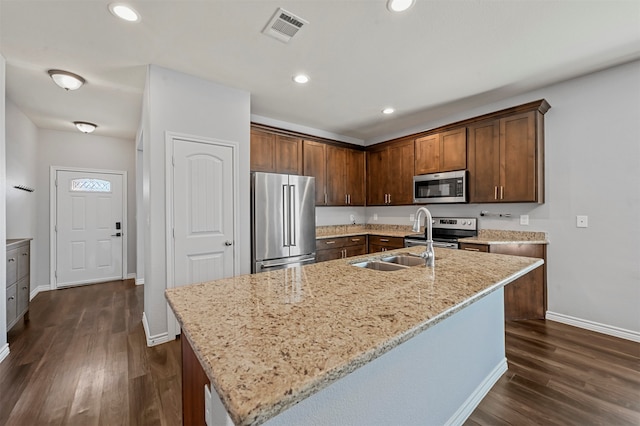 kitchen with stainless steel appliances, a center island with sink, and light stone counters