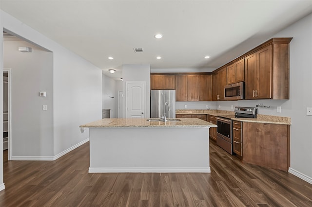 kitchen featuring light stone counters, an island with sink, stainless steel appliances, and dark hardwood / wood-style flooring