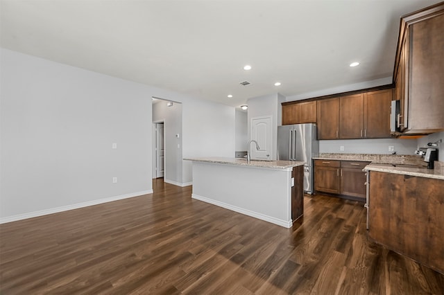 kitchen with dark wood-type flooring, an island with sink, appliances with stainless steel finishes, and light stone counters